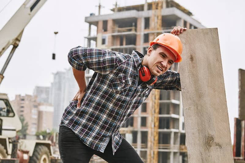 A construction worker grimacing from lower-back pain on a job site
