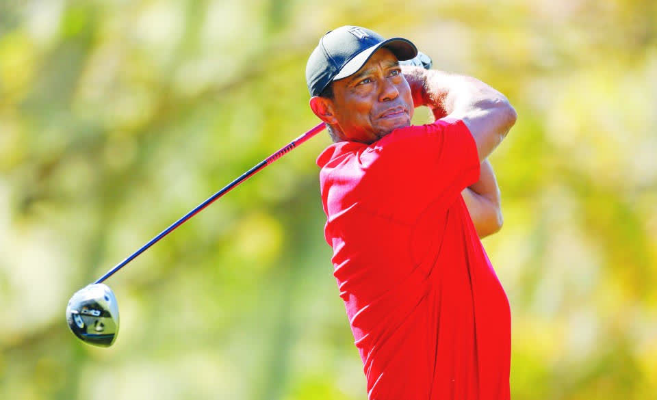 Tiger Woods follows through on a driver swing in his signature red Sunday shirt