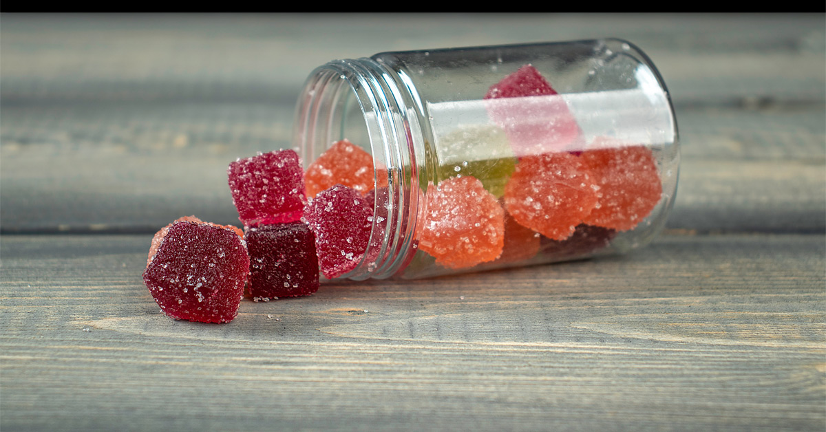 Green CBD gummies beside a dark green glass bottle